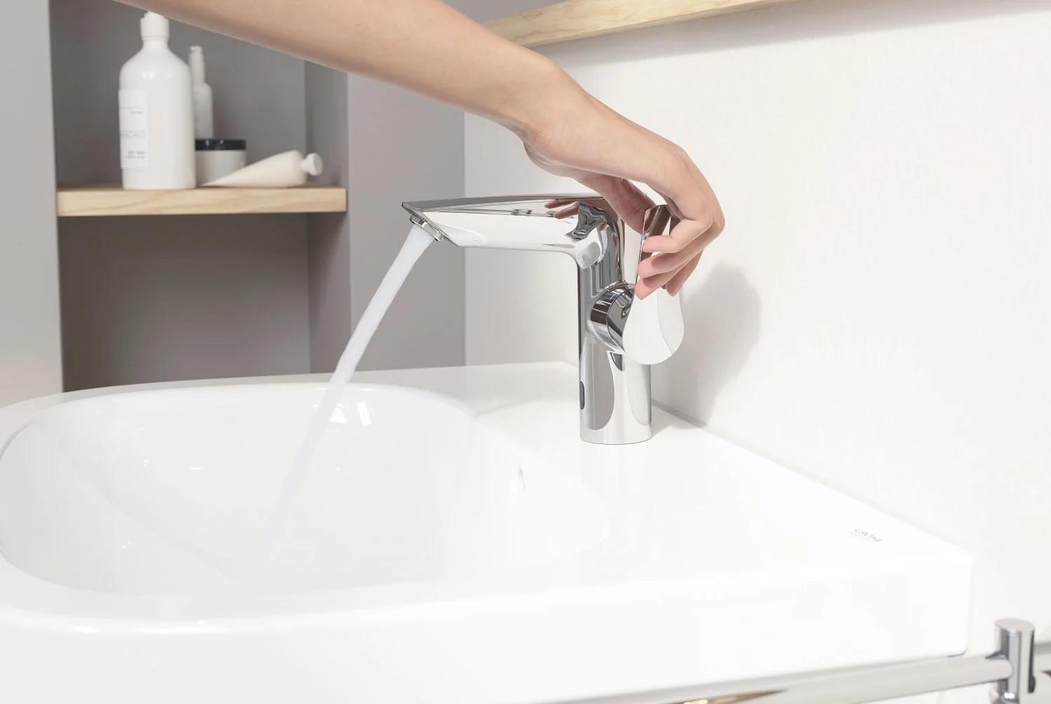 Ręka obsługująca chromowaną baterię umywalkową w łazience, Grohe