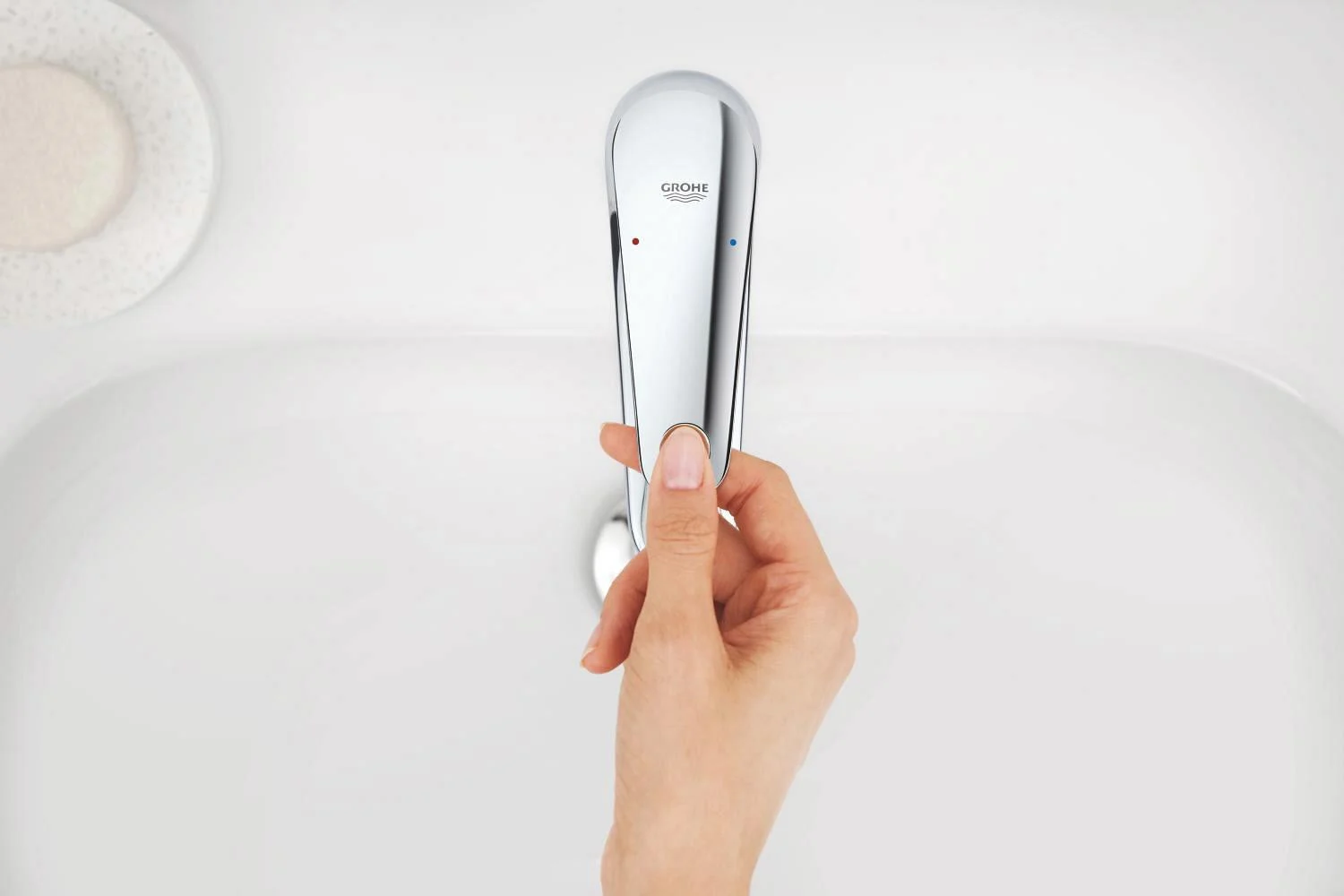 Ręka obsługująca chromowaną baterię umywalkową z góry, Grohe
