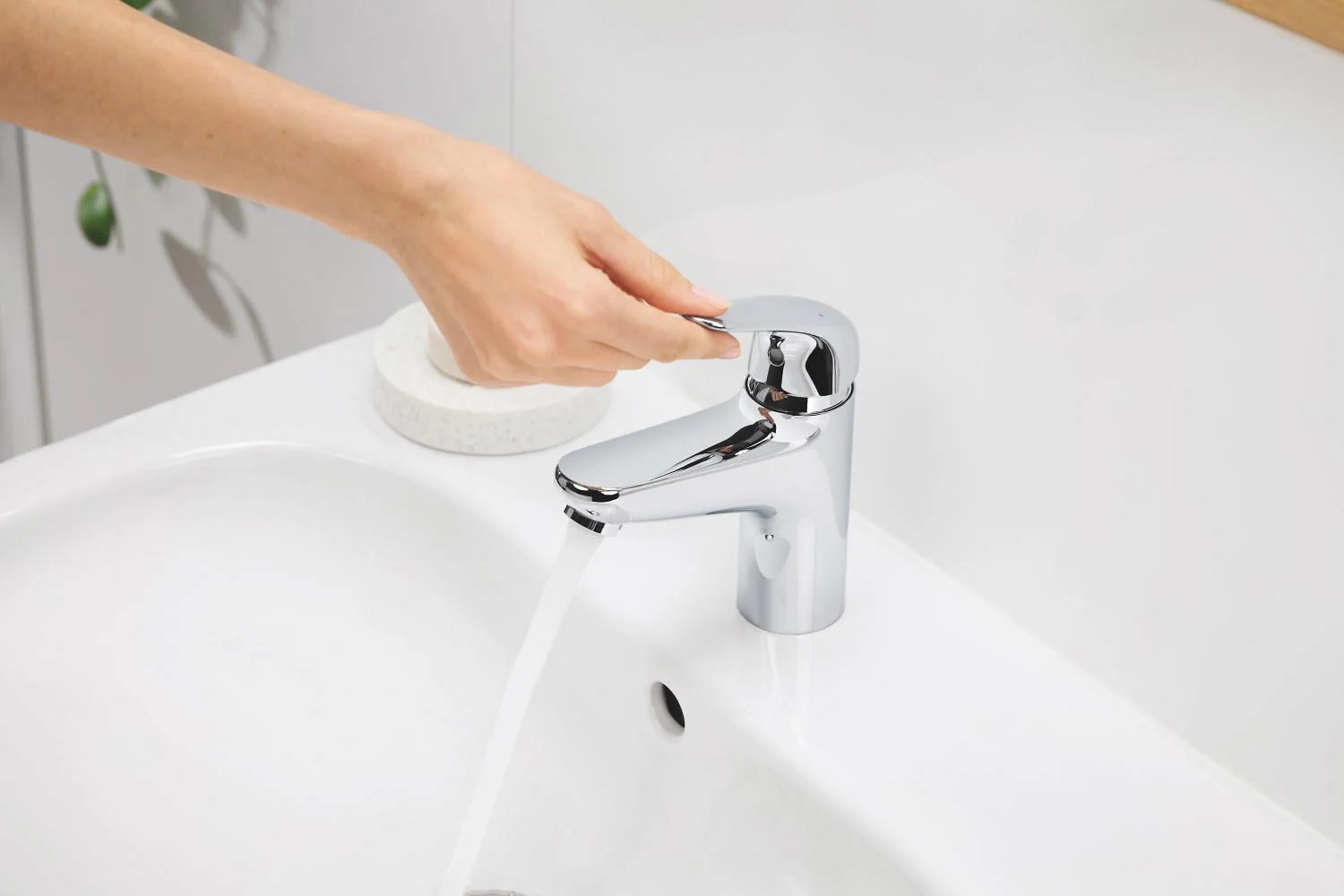 Ręka odkręca chromowaną baterię umywalkową w łazience, Grohe