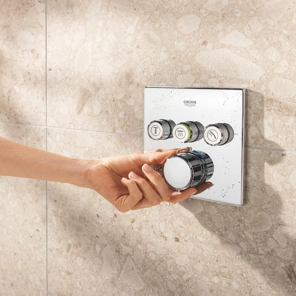 Ręka obraca okrągły regulator prysznicowy na ścianie z płytek, Grohe