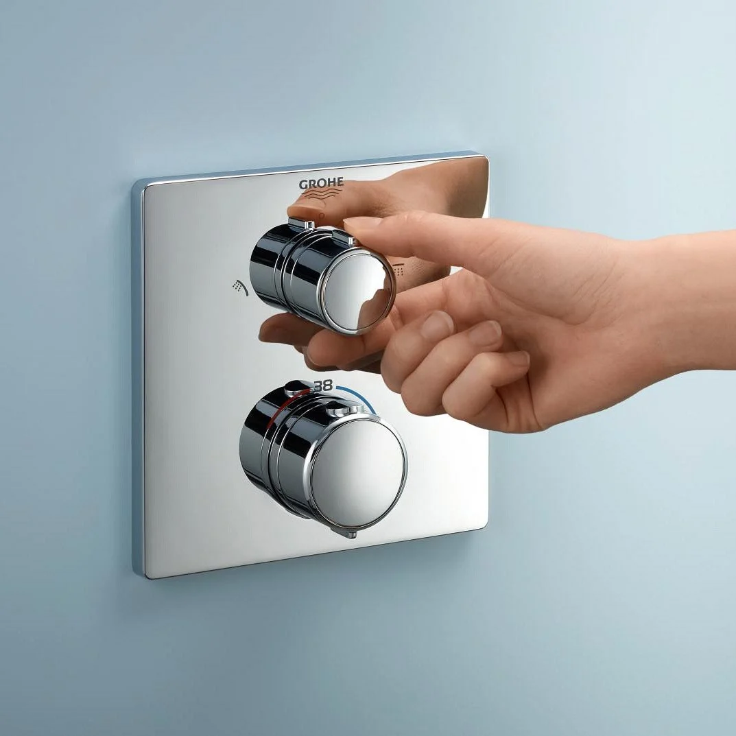 Ręka obsługuje okrągły regulator prysznicowy na niebieskiej ścianie, Grohe