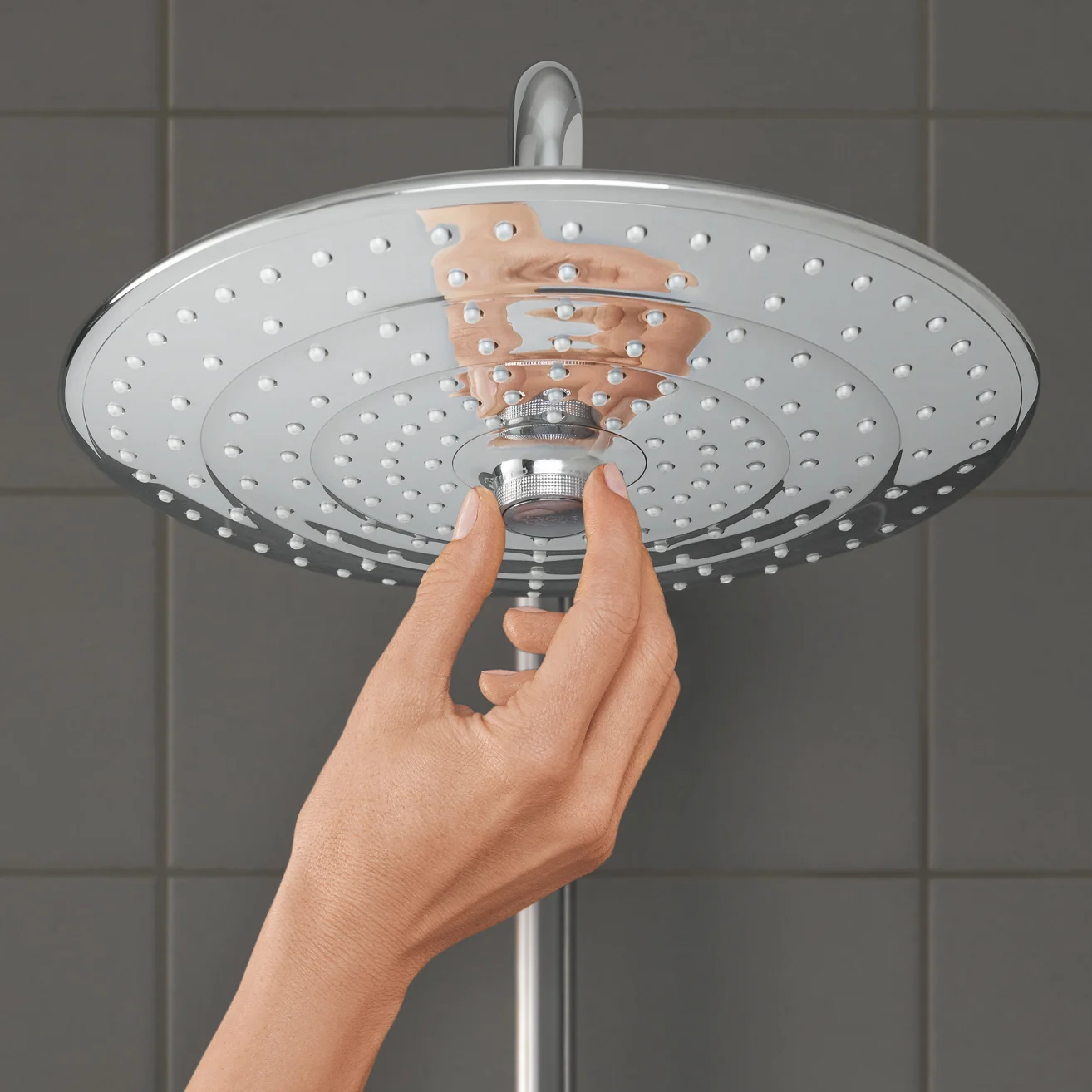 Ręka reguluje głowicę prysznicową, szare płytki, Grohe