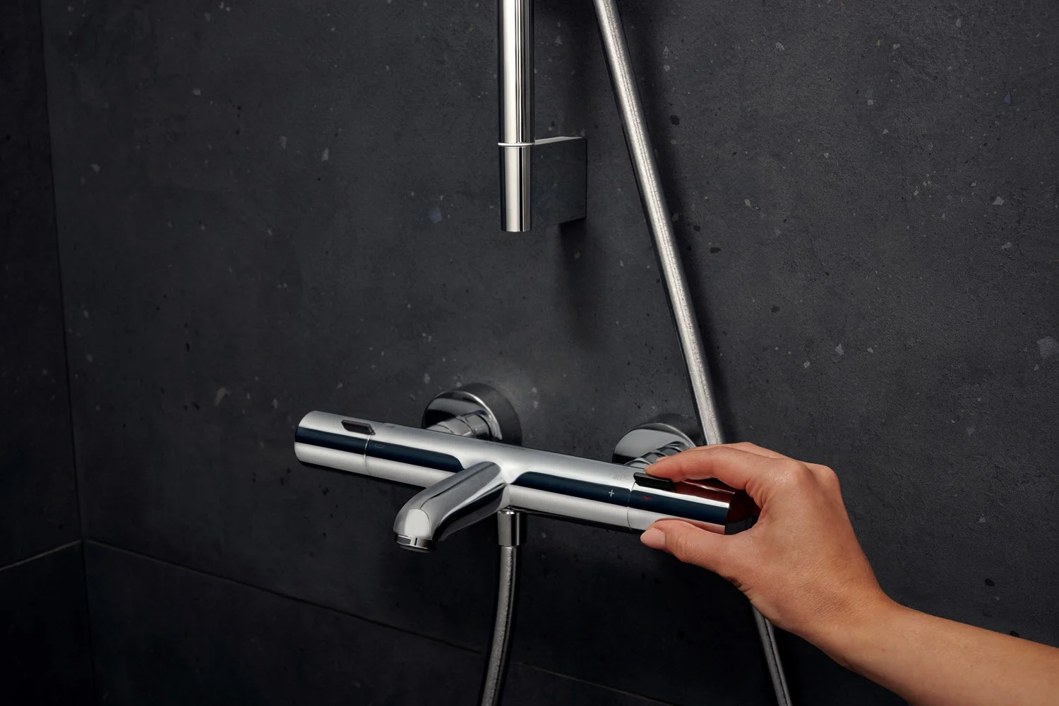 Ręka obsługuje srebrny termostat prysznicowy na ścianie, hansgrohe