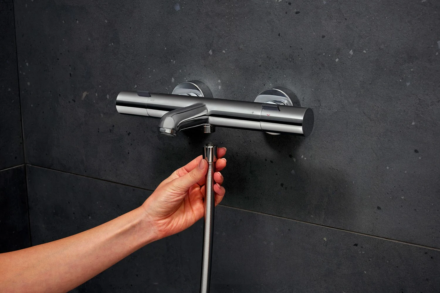Ręka reguluje srebrny termostat prysznicowy na ścianie, hansgrohe