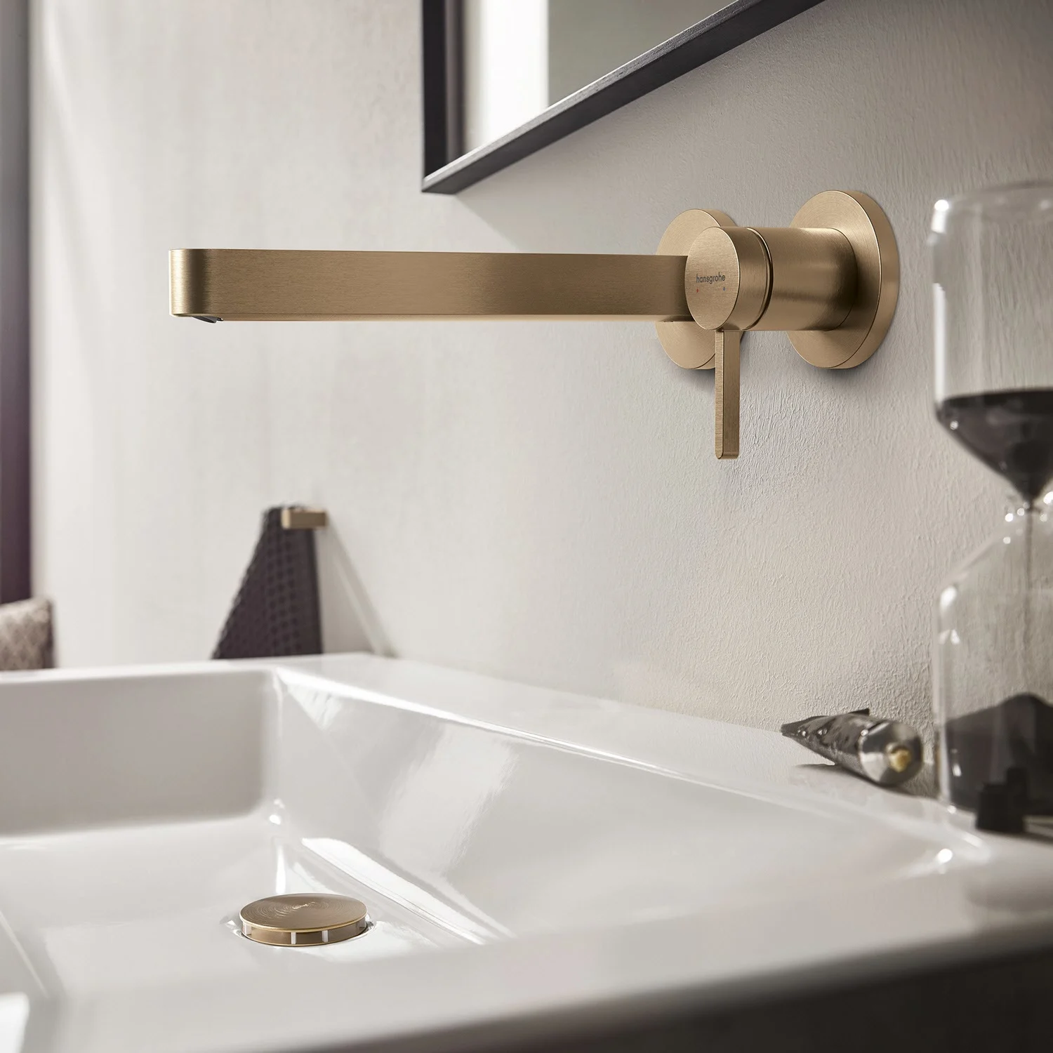 Złota bateria ścienna nad białą umywalką, hansgrohe
