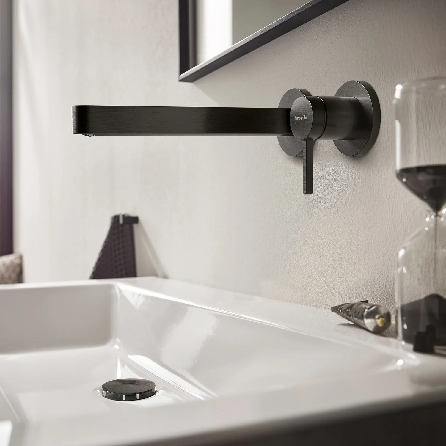 Czarna bateria ścienna nad białą umywalką, hansgrohe