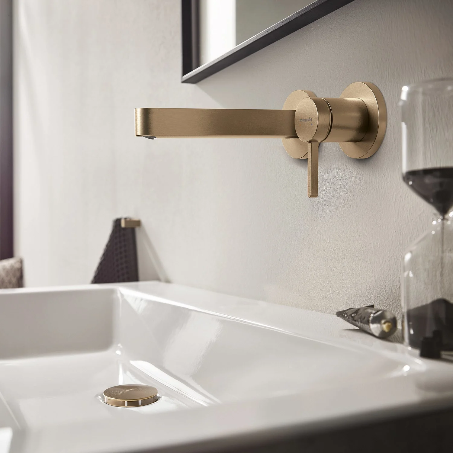 Złota bateria ścienna nad białą umywalką, hansgrohe