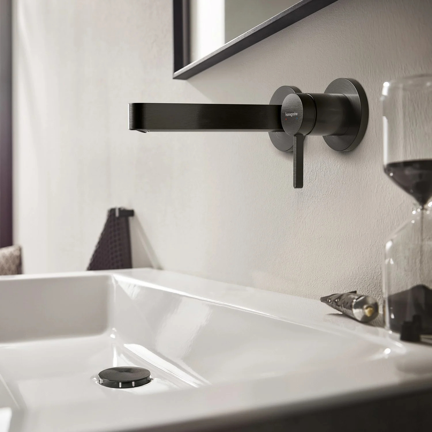 Czarna bateria ścienna nad białą umywalką, hansgrohe