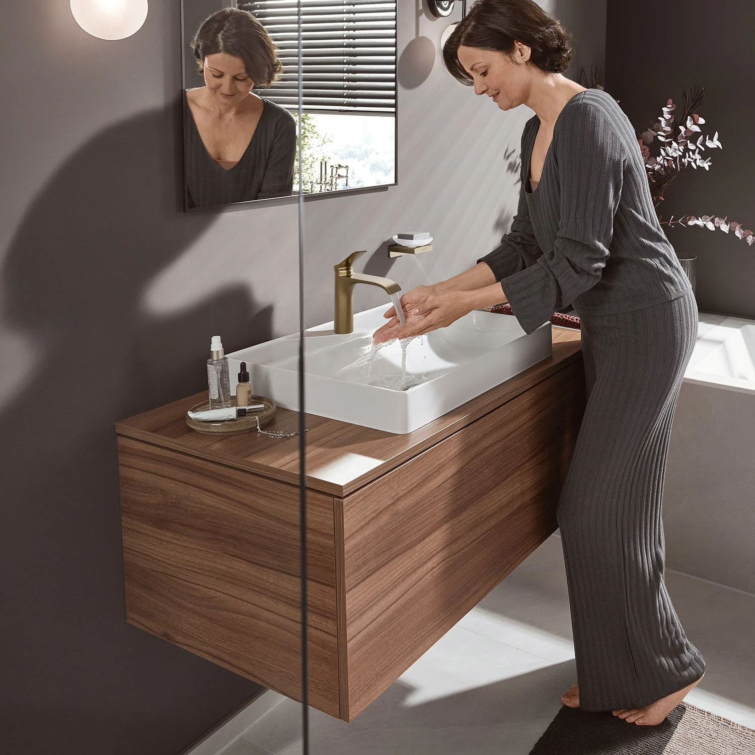Kobieta używa umywalki ze złotą baterią, hansgrohe