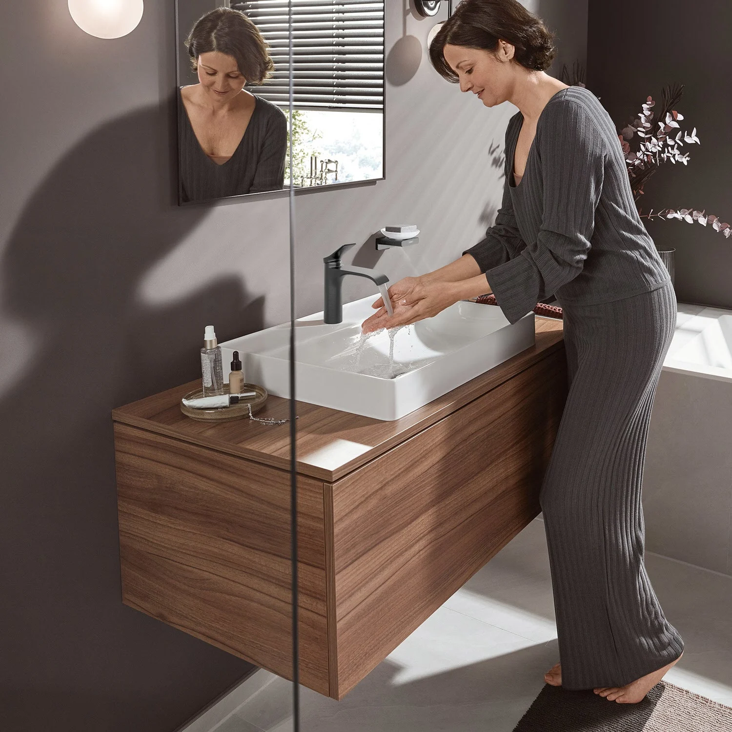 Kobieta używa umywalki z czarną baterią, hansgrohe