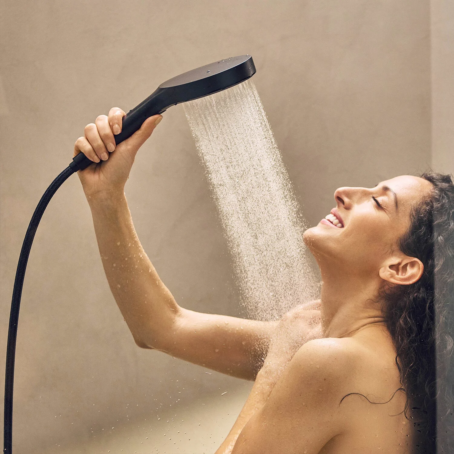Osoba pod prysznicem z czarną słuchawką prysznicową, hansgrohe