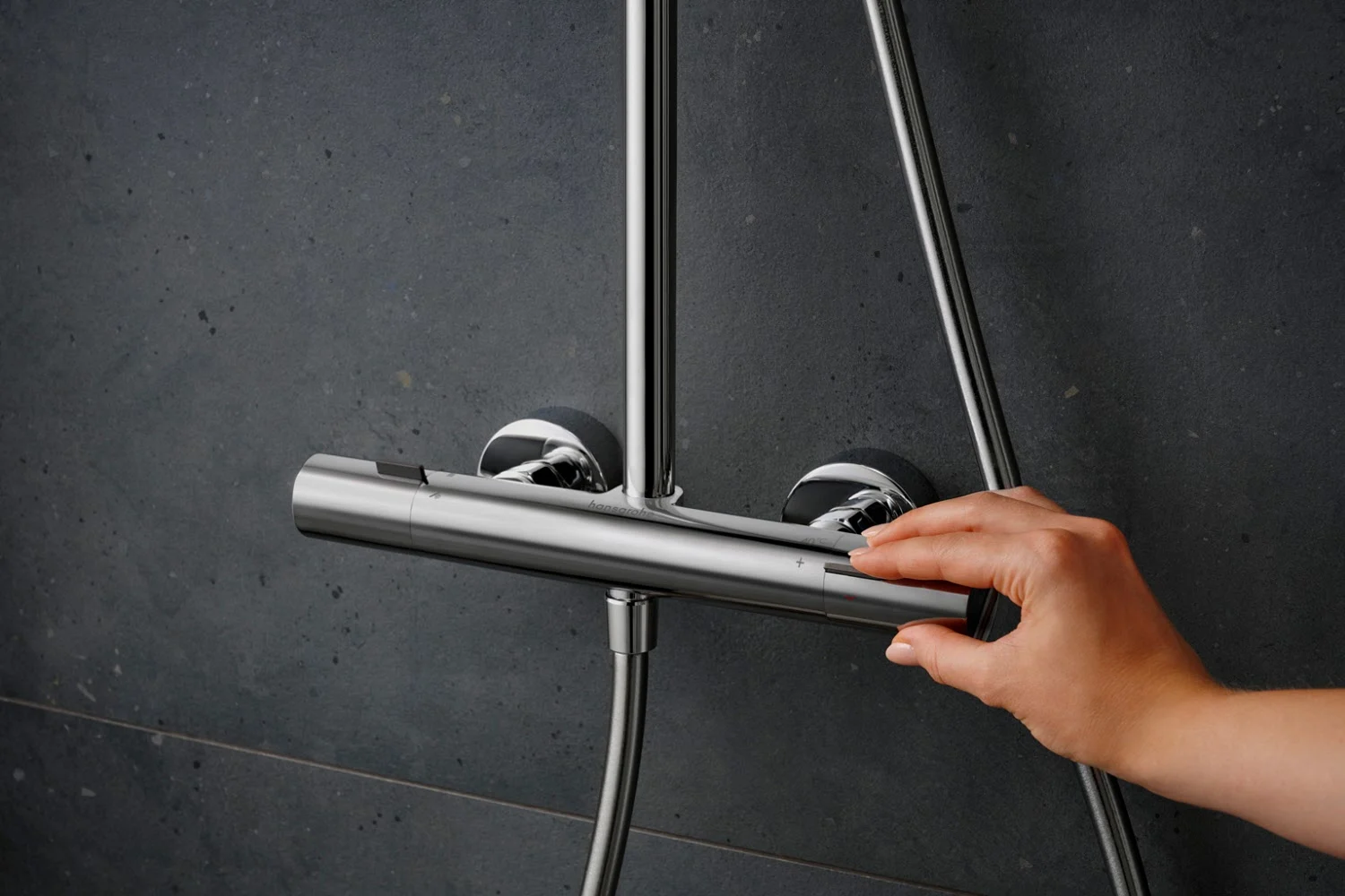 Ręka dotyka armatury prysznicowej na ciemnej ścianie, hansgrohe