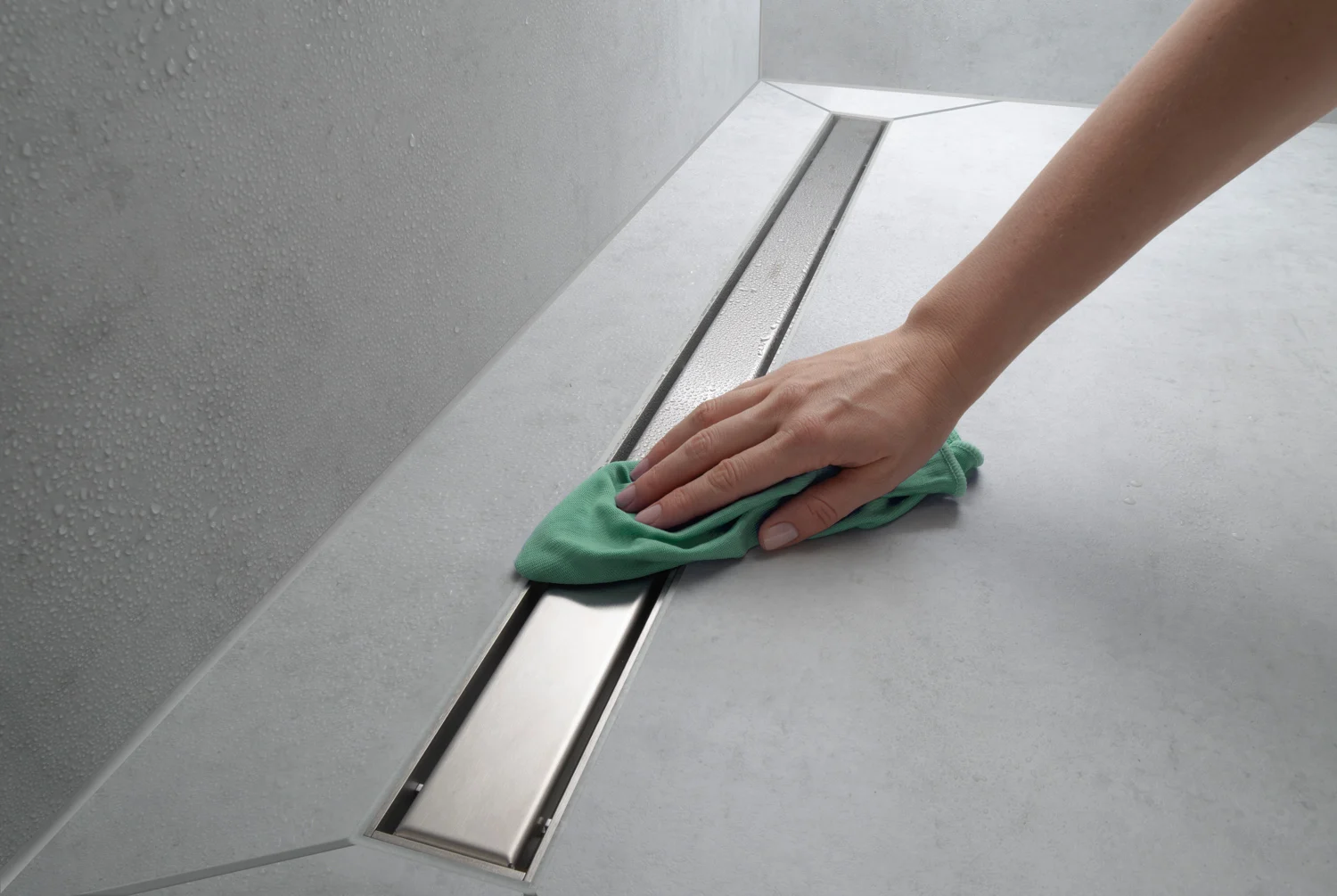 Ręka czyszcząca pokrywę odpływu prysznicowego zieloną szmatką, hansgrohe