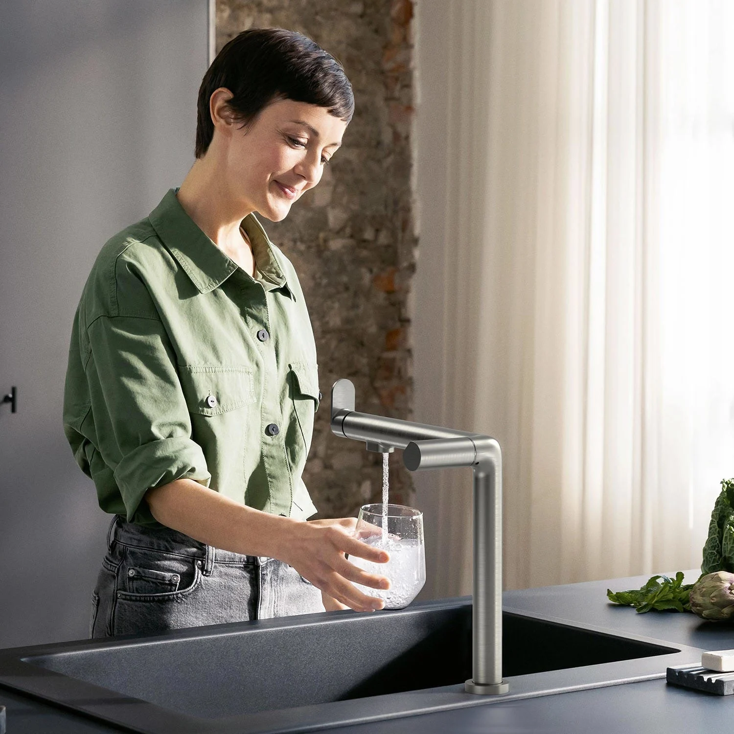 Osoba napełnia szklankę przy stalowej baterii kuchennej, hansgrohe