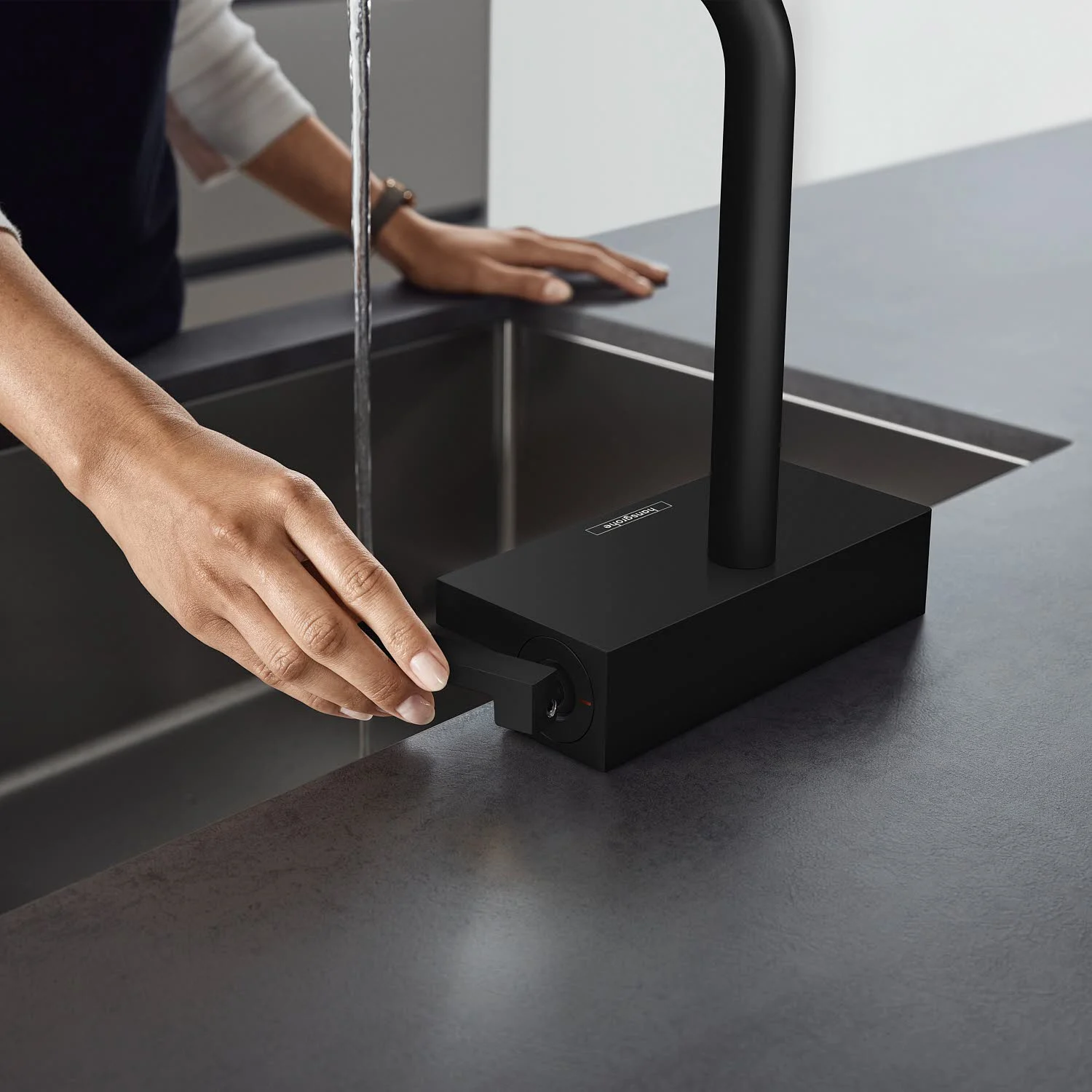Osoba obsługuje czarną baterię kuchenną przy zlewie, hansgrohe