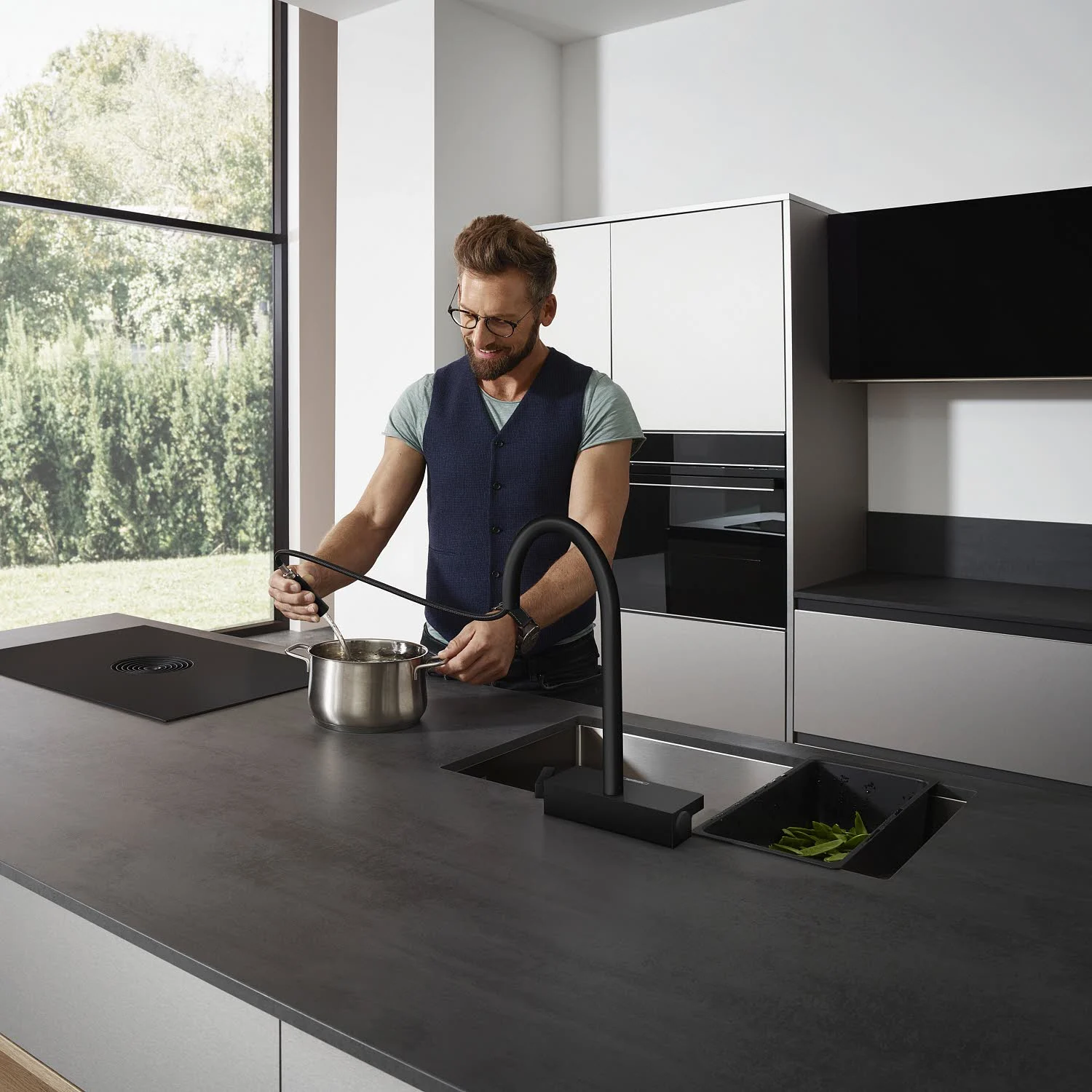Mężczyzna gotuje z czarną baterią kuchenną w nowoczesnej kuchni, hansgrohe