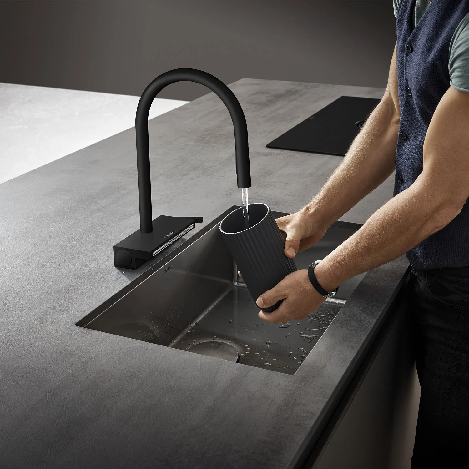 Mężczyzna napełnia pojemnik wodą z czarnej baterii kuchennej, hansgrohe