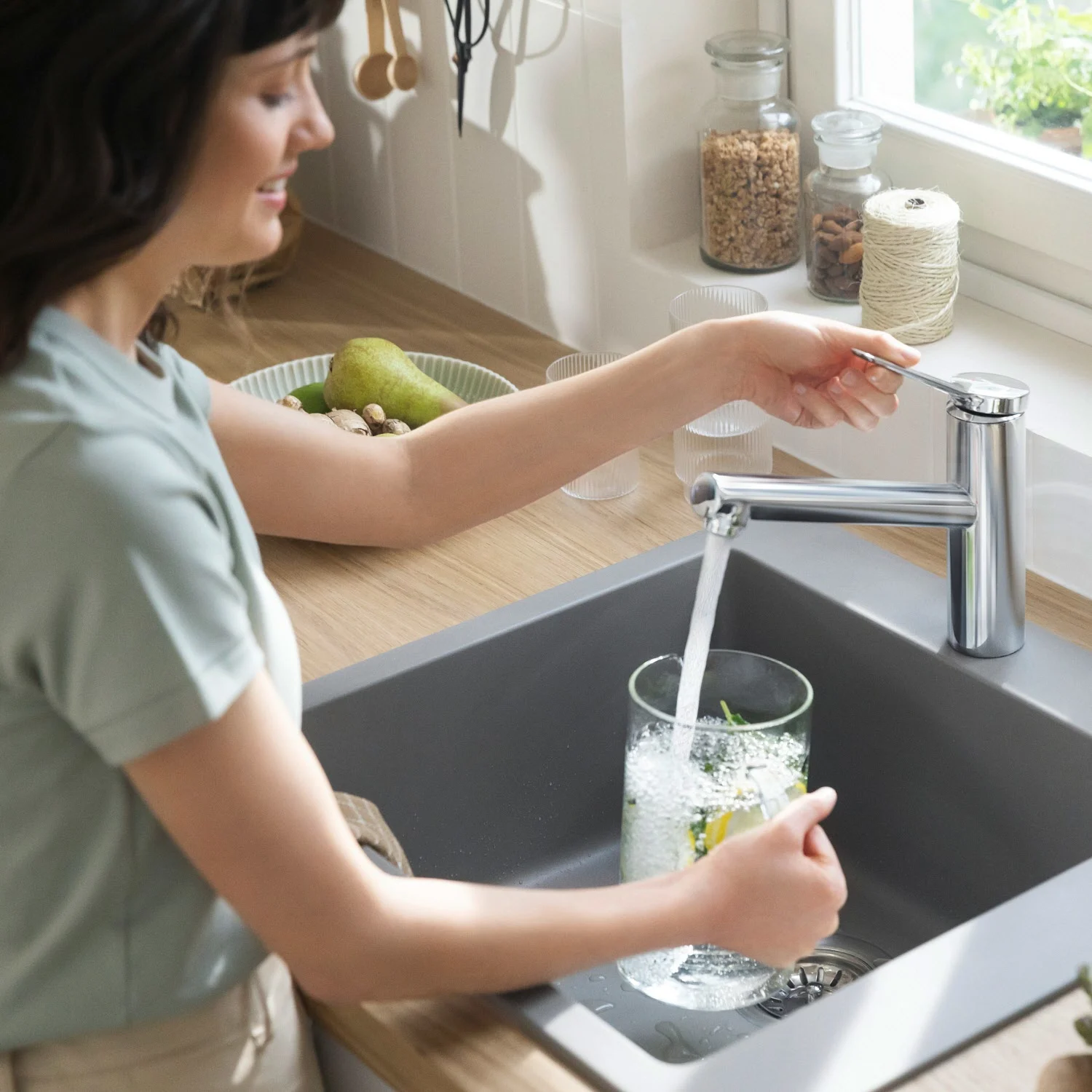 Kobieta używa baterii kuchennej ze szklanką wody z bliska, hansgrohe