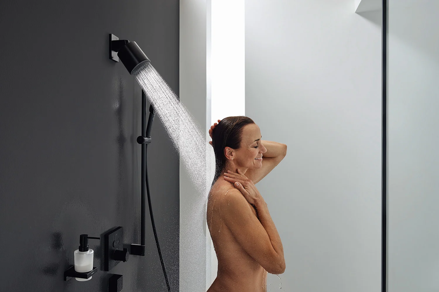Osoba pod prysznicem z czarną głowicą prysznicową, hansgrohe