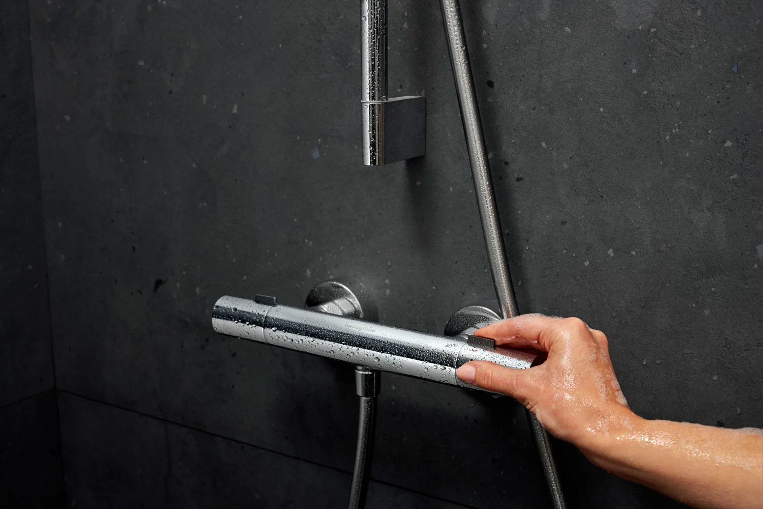Ręka reguluje srebrny termostat prysznicowy na ścianie, hansgrohe