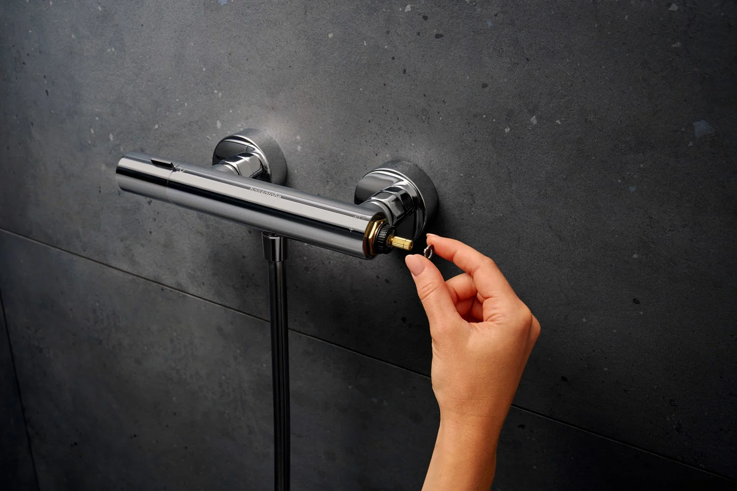 Ręka montuje termostat na ciemnej ścianie, hansgrohe
