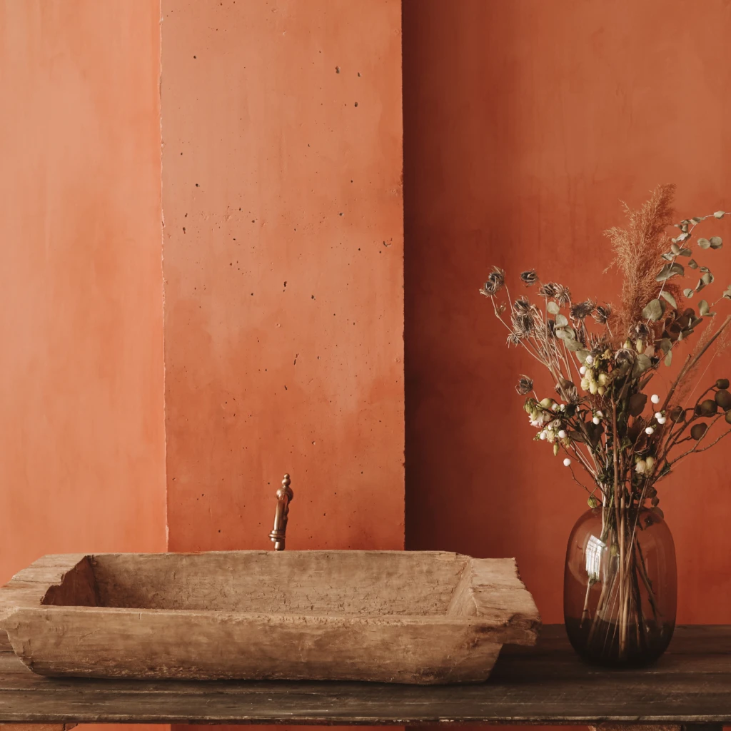 rustikales Holzwaschbecken neben einer Vase mit Trockenblumen vor einer orangener Wand