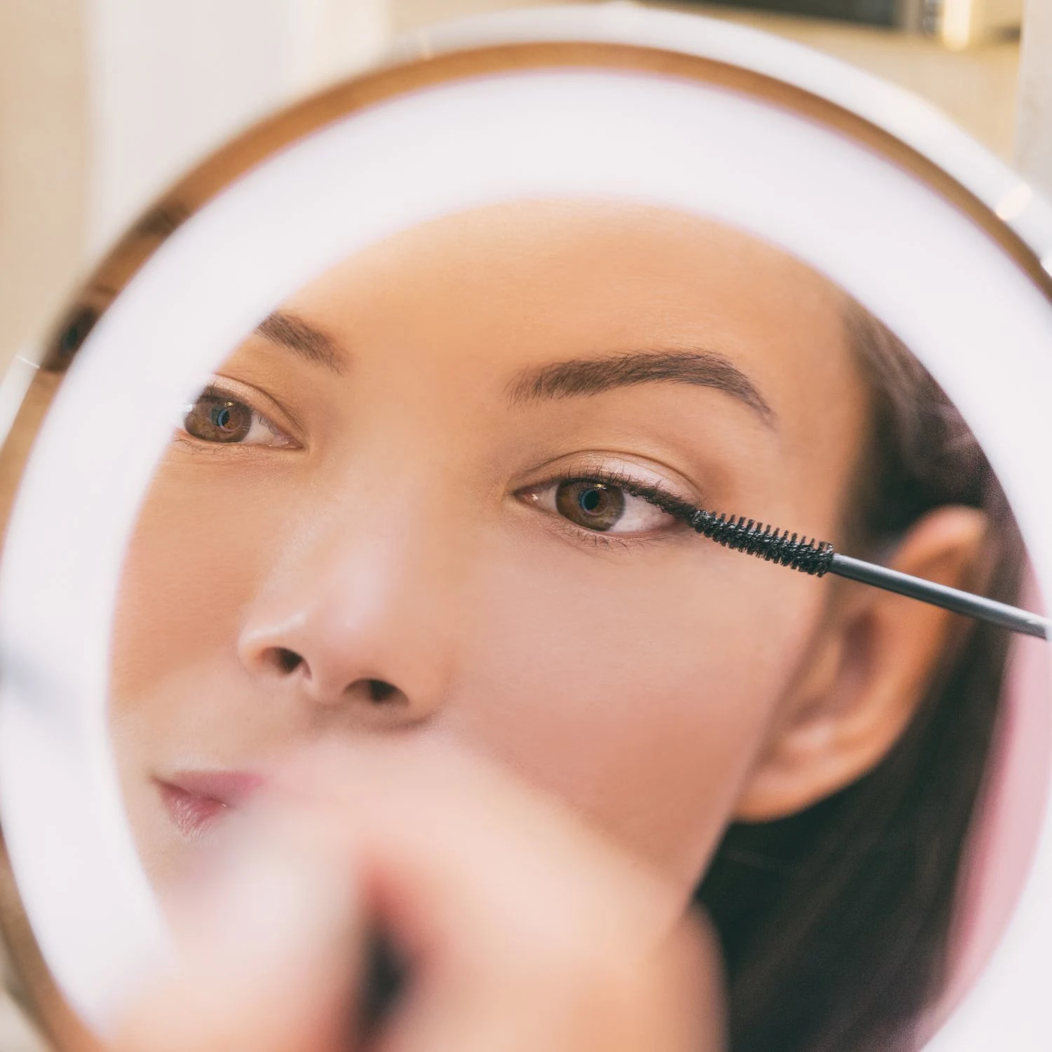 Frau schaut während dem Schminken in einen Kosmetikspiegel mit Vergrößerung