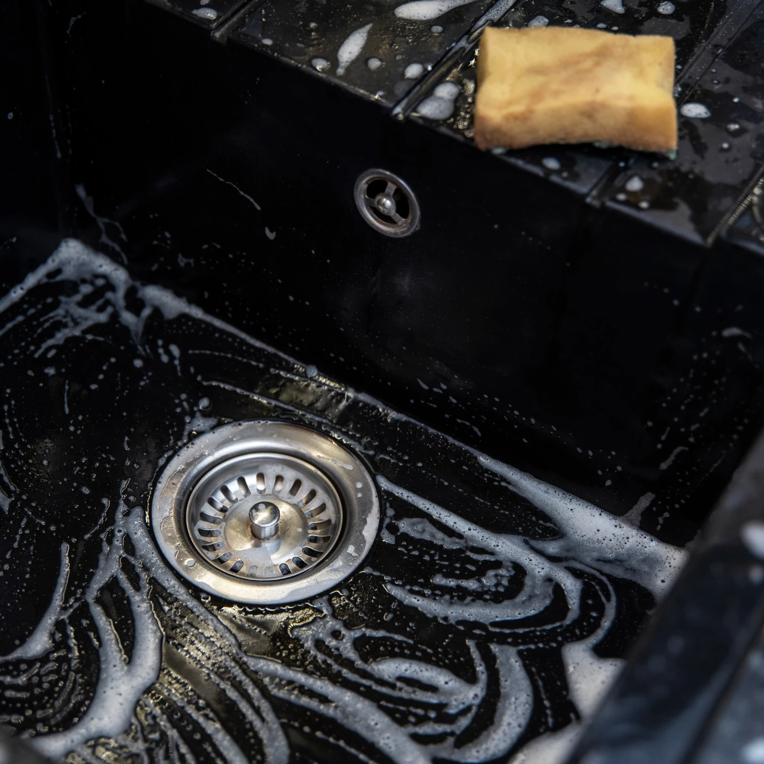 Schwarze Spüle mit Schaum und einem gelben Schwamm