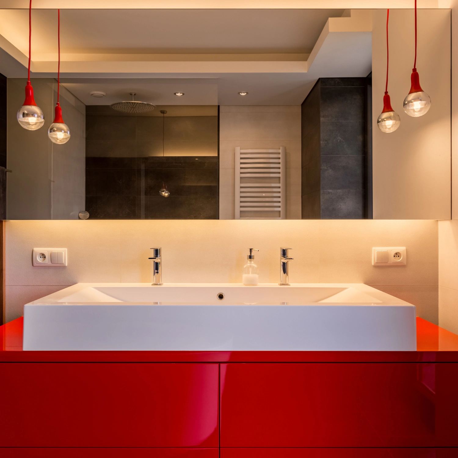 modernes Badezimmer mit roten Hängelampen und einem rot-glänzendem Waschtischunterschrank