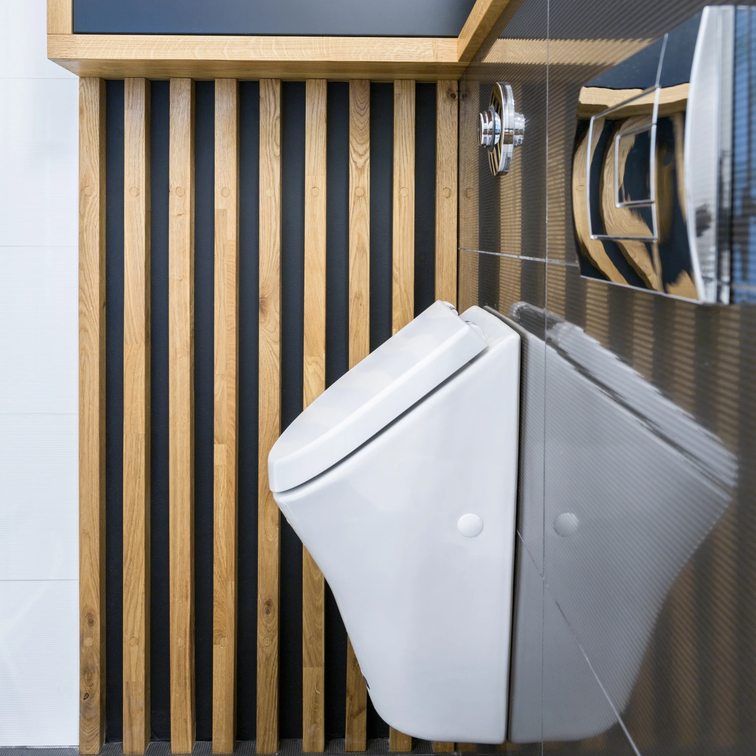 weißes Urinal vor dunklen Fliesen und Holzverkleidung an der Wand