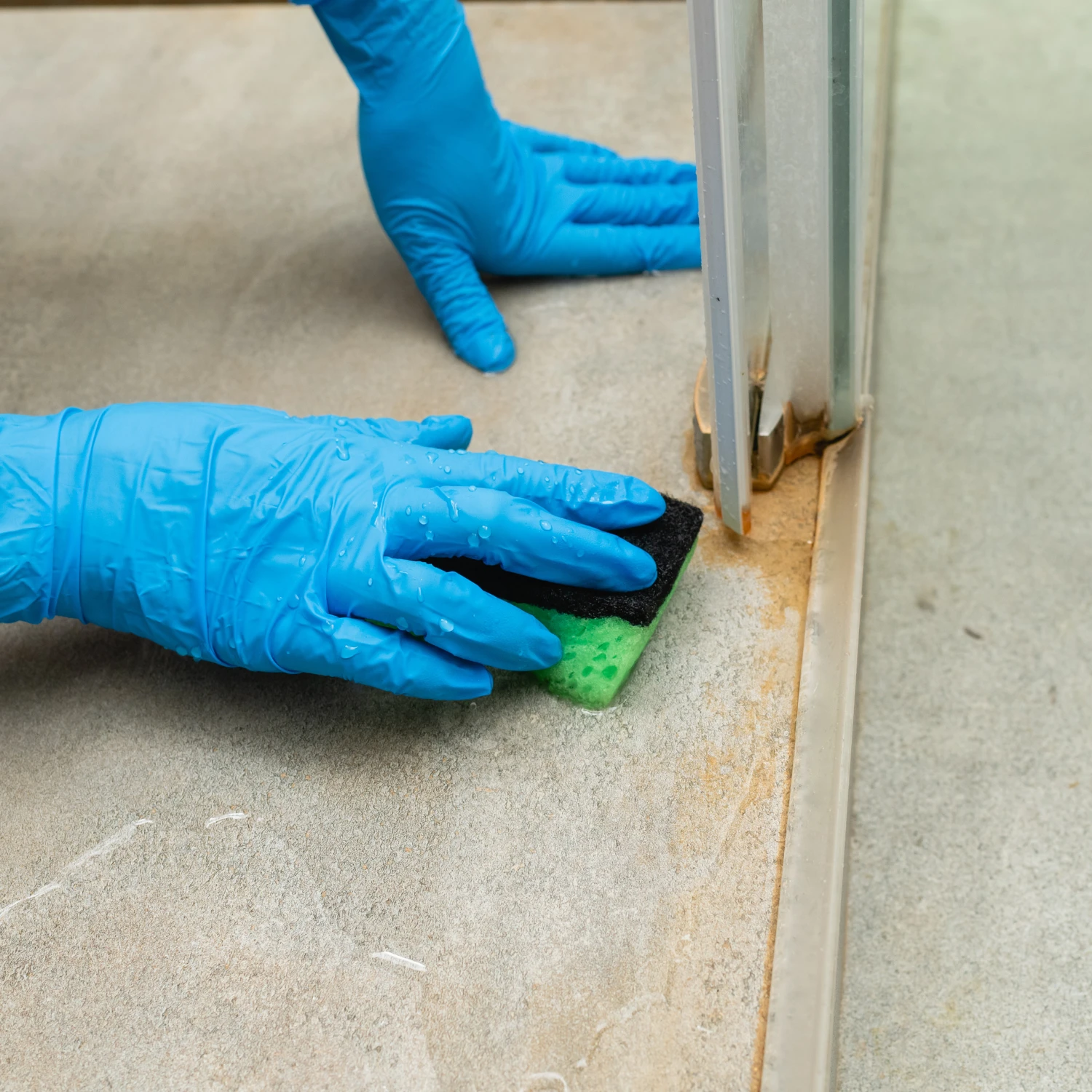 Mit einem grünen Schwamm werden Kalk- und Schmutzablagerungen am unteren Rand der Duschkabine entfernt.