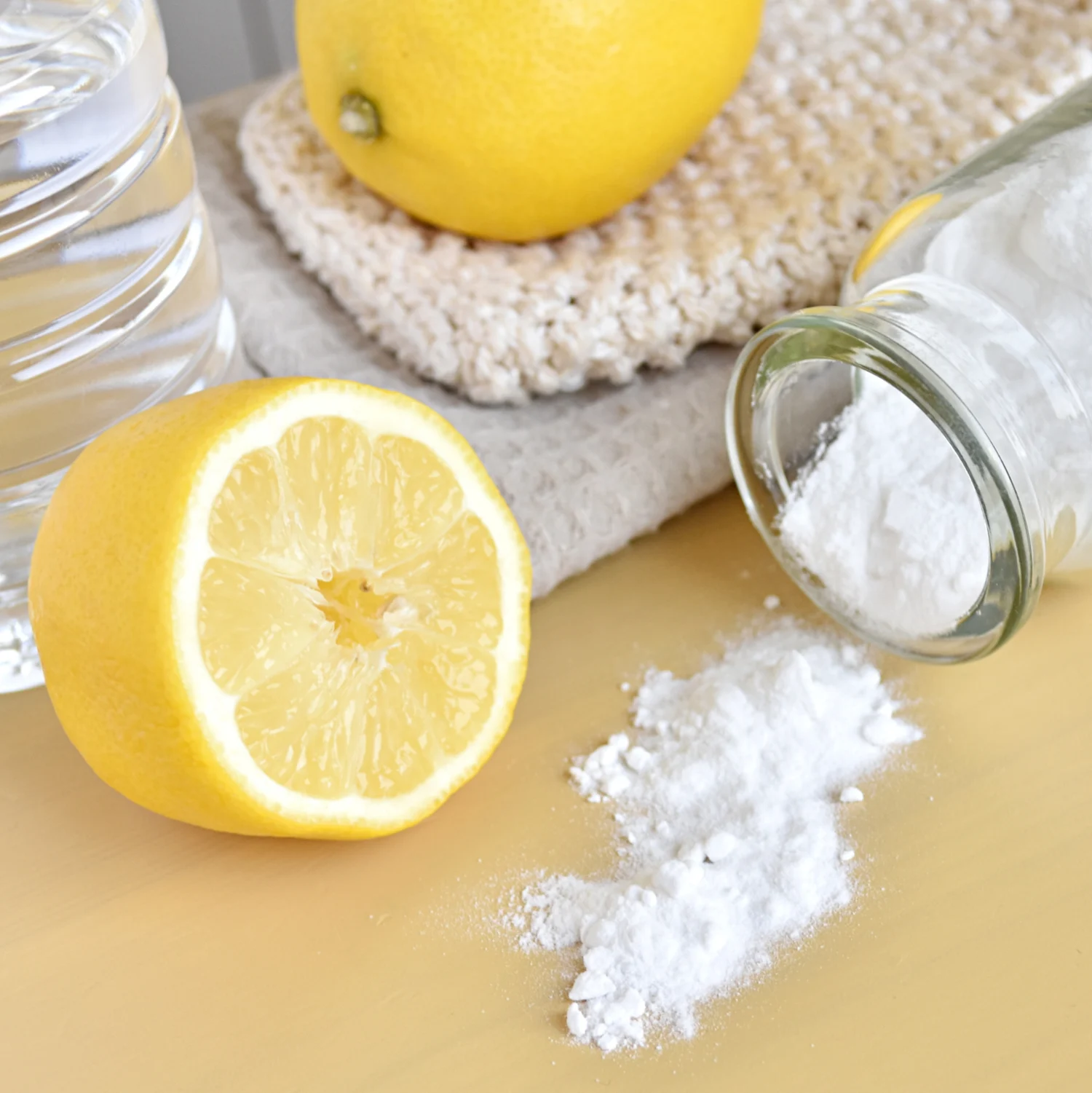 Aufgeschnittene Zitrone neben Backpulver und einer Flasche Essig auf einem Holztisch