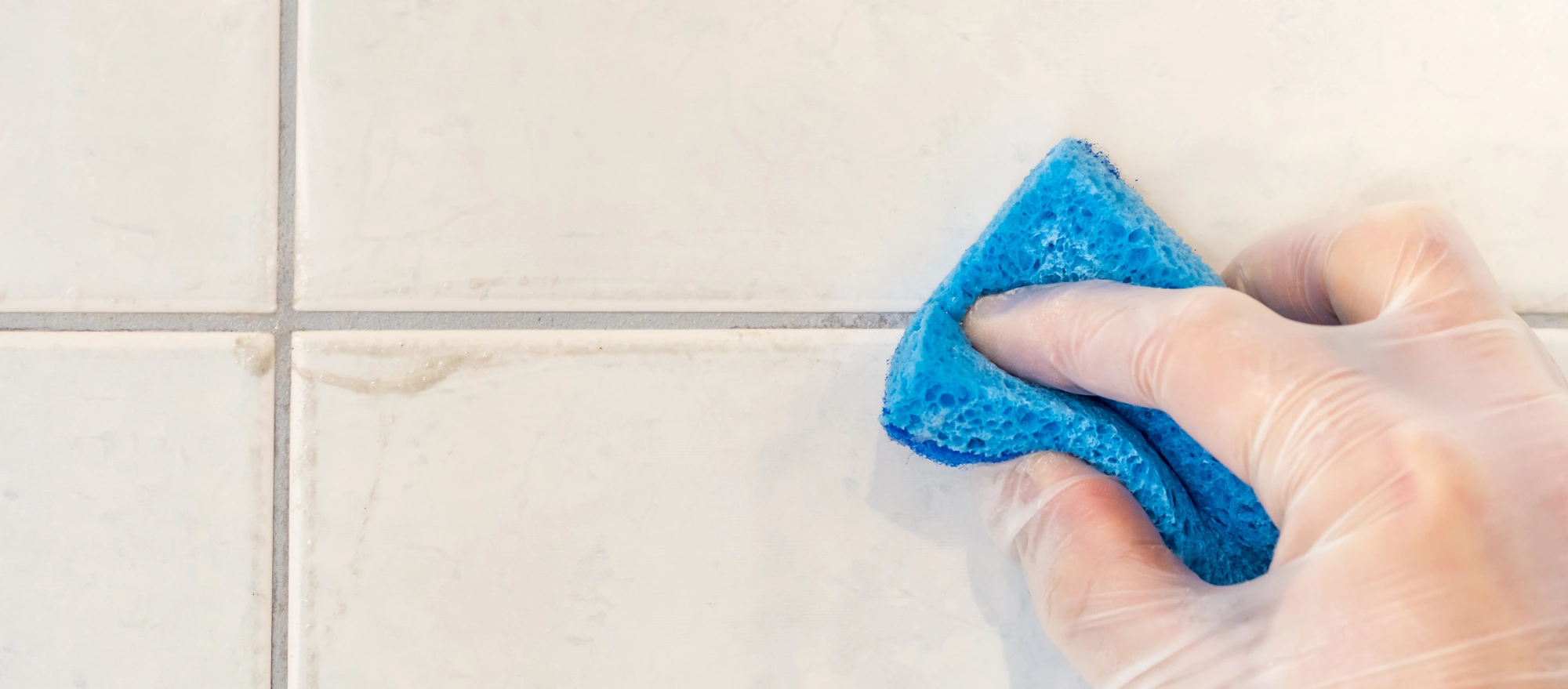 Schmutzige Fugen werden mit Hilfe eines blauen Schwamms gereinigt.