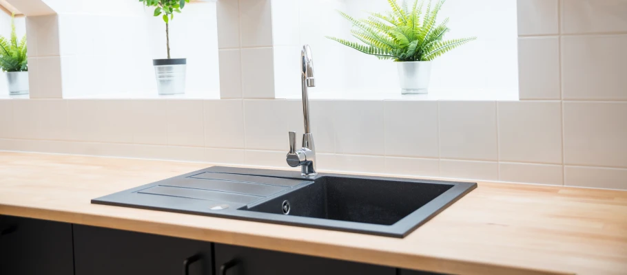 Schwarze Spüle mit chromfarbender Armatur in einer hellen Küche mit einer Arbeitsplatte aus Holz